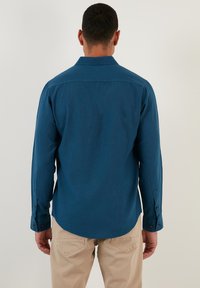 Blauwe lange mouwen shirt van gladde stof met een kraag, knoopmanchetten en een gebogen zoom. Draag het met lichtbeige broek.
