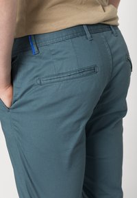 Pantalons en coton bleu avec une texture lisse, dotés d'une poche arrière et de détails cousus. La taille a un accent bleu contrastant.