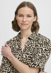 Košeľa s leoprintom, ktorá má golier na gombíky, krátke rukávy a voľný strih. Materiál vyzerá ľahký s hladkou textúrou.