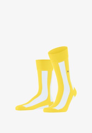 Gele enkelsokken met witte verticale strepen en een klein rond metalen logo aan de zijkant, naast elkaar weergegeven op een witte achtergrond.