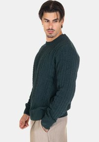 Maglione a coste in verde scuro con scollo rotondo, polsini e orlo a costine, superficie testurizzata e vestibilità ampia.