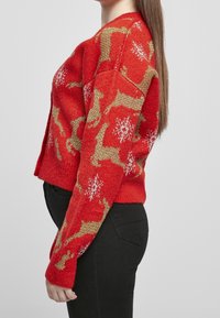 Roter Strickpullover mit Rentier- und Schneeflockenmuster in Gold und Weiß. Kurzer Schnitt mit langen Ärmeln und geripptem Saum.