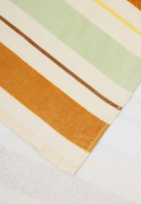 Pruhovaná tkanina v farbách ako zelená, oranžová, hnedá a smotanová. Mäkká textura a viditeľné prešitie na okraji.