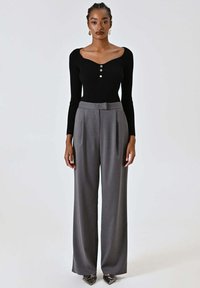 Top nero a maniche lunghe a coste con tre bottoni, abbinato a pantaloni grigi a gamba larga e a vita alta. La modella indossa tacchi metallici appuntiti.