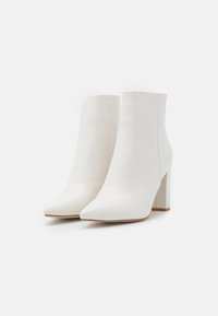 Białe botki za kostkę z szpiczastym noskiem, wykonane z gładkiej skóry. Posiadają masywny, wysoki obcas oraz jednolitą konstrukcję z minimalną ilością szwów.