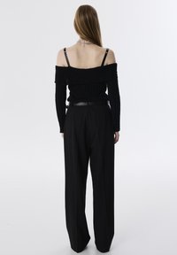 Zwarte off-shoulder ribbed trui met lange mouwen, gedragen met hoge taille zwarte ruime broek en een slanke zwarte riem.