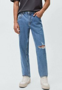 Light blue denim jeans with a relaxed fit, featuring a distressed knee detail. Paired with white sneakers and a dark gray shirt.