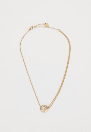 Gouden ketting met twee schakels, voorzien van een ronde hanger versierd met kleine, heldere stenen en een letter "G" in het midden.