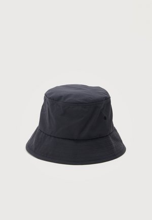 Schwarzer Stoff-Bucket-Hut mit breiter, gesteppten Krempe und Belüftungsösen vor hellem, einfarbigem Hintergrund.