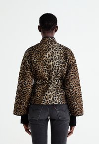 Leopardprint jas met een ceintuur in de taille, lange mouwen en een gestructureerde stof. Het ontwerp bevat opvallende zwarte en gouden vlekken op een beige achtergrond.