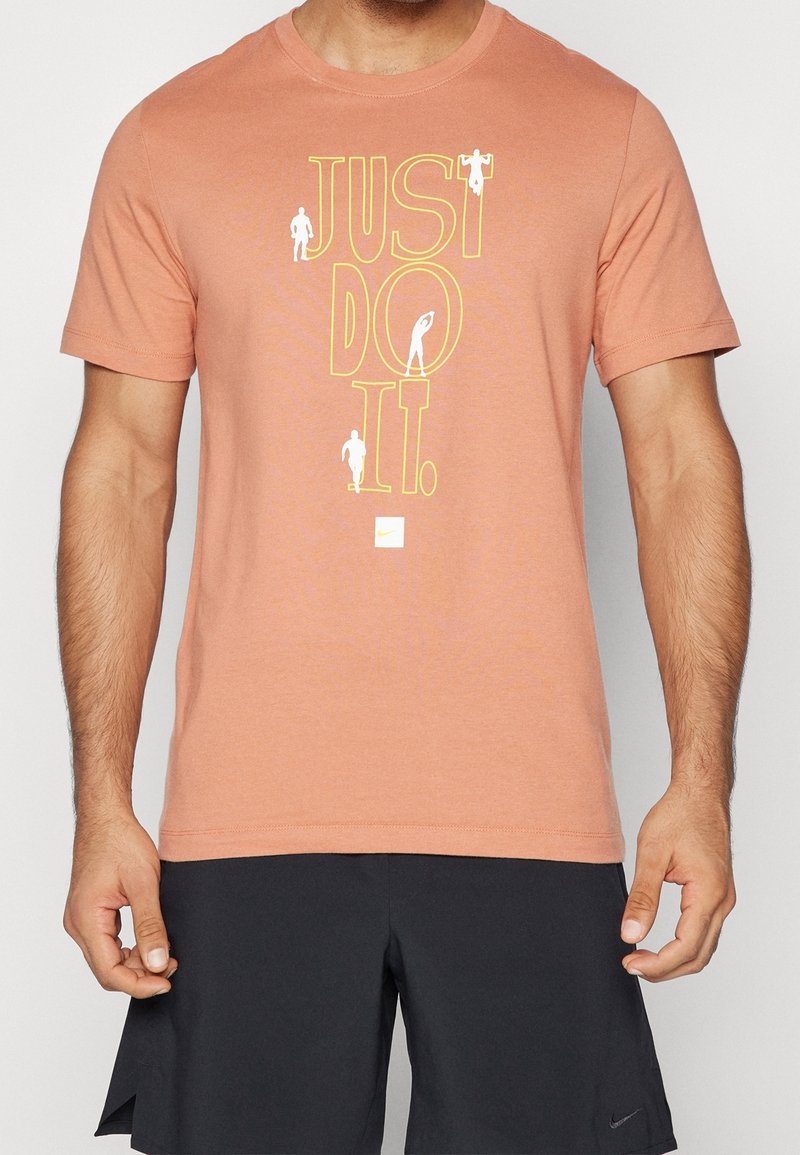 Koraal kleurige T-shirt met korte mouwen, gemaakt van een katoenmengsel. Bevat grote gele tekst "JUST DO IT." en een klein Nike-logo. Eenvoudig ontwerp zonder patronen.