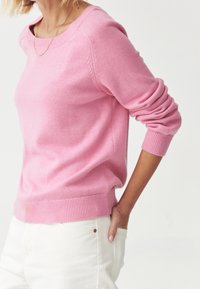 Růžový svetr vyrobený z jemného materiálu, s kulatým výstřihem, žebrovanými manžetami a lemem. Hladká textura s jemným švem na ramenou.