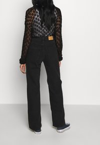 Pantalones de mezclilla anchos negros con cintura alta, que presentan una etiqueta de cuero en la parte trasera y zapatillas casuales. La parte superior es de un tejido de punto negro y texturizado.