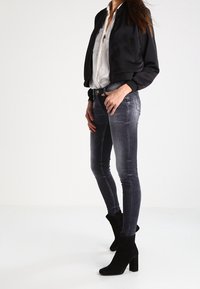 Black bomber jacket over a white shirt, paired with slim-fit gray jeans and black suede ankle boots. Focus on fabric and fitted design.