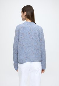 Camisola de malha azul claro com padrão texturizado e salpicos de cor. Apresenta gola redonda e punhos e bainha canelados.