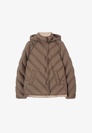 Femme portant une doudoune matelassée taupe par-dessus un pull à col roulé beige, ajustant le col de la veste avec la main.