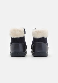 Botine bleumarin cu guler din blană sintetică, cu toc din piele netedă și corp din suede. Logo pe toc. Închidere cu eșarfă sigură.