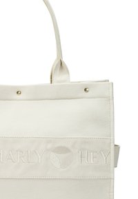Beige stoffen tote bag met twee lus handvatten, met op de voorkant een reliëf merknaam "Marly Hey" en een cirkelvormig logo.