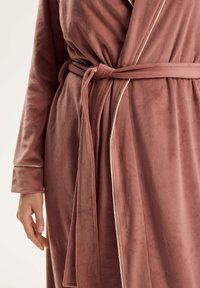 Fioletowy, miękki szlafrok z regulowanym związaniem. Posiada długie rękawy oraz kontrastowe białe obszycia na brzegach jako detal akcentujący.