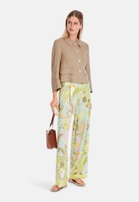 Beige linen jacket with a collared neckline, paired with light, floral-patterned wide-leg trousers. Model holds a brown handbag.
