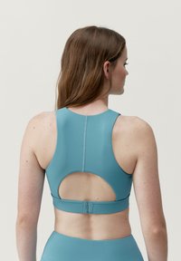 Tealfärgad sport-bh med hög halsringning, racerback-design och utskärning på baksidan. Har ett mjukt, elastiskt tyg med minimala sömmar.