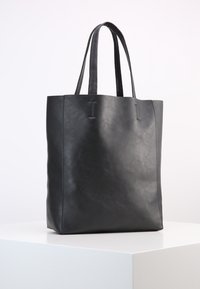 Černá kožená taška s dvěma dlouhými ušima, minimalistický design, obdélníkový tvar, hladká textura a jemné švy.