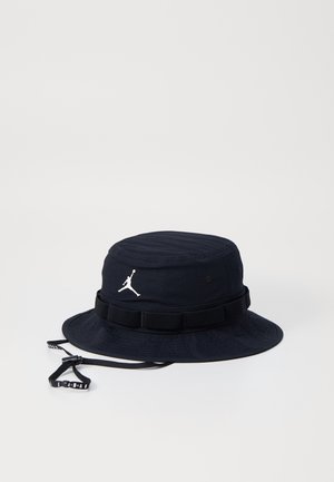 Czarny kapelusz typu bucket z szerokim rondem, regulowanym paskiem pod brodą i białym logo Jumpman z przodu na jednolitym tle.