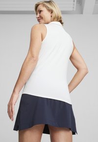 Bezrukávový polokošeľa v bielej farbe s golierom, skombinovaný s námorníckou sukňou. Tkanina sa zdá byť hladká s jemným leskom a má vrstvený dizajn.