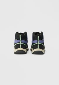 Zapatos deportivos de caña alta en negro y morado con parte superior de tela texturizada, acentos en verde claro y suela de goma beige resistente.