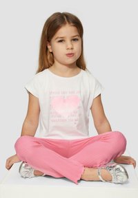 Witte T-shirt met een roze bedrukte hart en tekst, gecombineerd met roze geribbelde broek en zilveren ballerina's. Eenvoudig ontwerp, casual pasvorm.