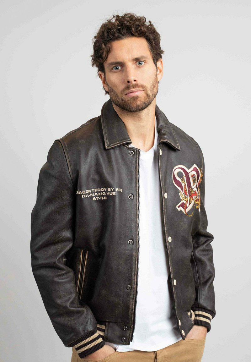 Veste de bombardier en cuir noir avec un détail de dragon brodé, des poignets côtelés et des rayures crème. Dotée de boutons-pression et d'un design vintage.