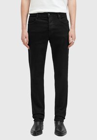 Jeans de mezclilla negra con un corte recto, cinco bolsillos y cierre de botón. Llevados con botas de tobillo de cuero negro.