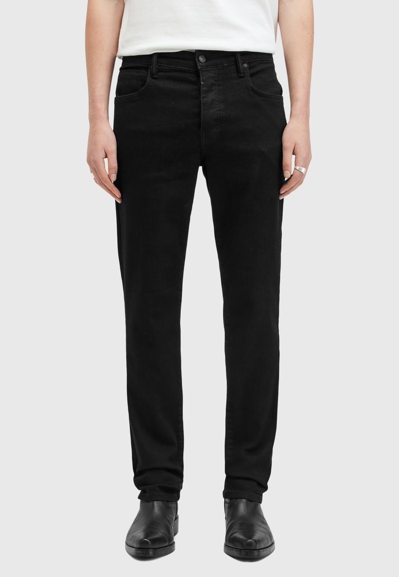 Jeans de mezclilla negra con un corte recto, cinco bolsillos y cierre de botón. Llevados con botas de tobillo de cuero negro.