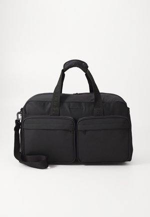 Black soft travel bag with two front zip pockets, dual handles with padded grip, and an adjustable shoulder strap against a white background.