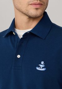 Marine polo shirt van textuurstof, met een spitse kraag, twee knopen en een lichtblauw geborduurd logo op de linkerborst.