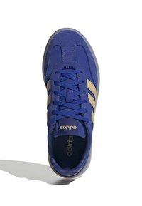 Modrá atletická bota se zlatými pruhy, textilní svršek, zavazování na tkaničky a gumová podrážka. Výrazné logo blízko jazyka a polstrovaný límec.