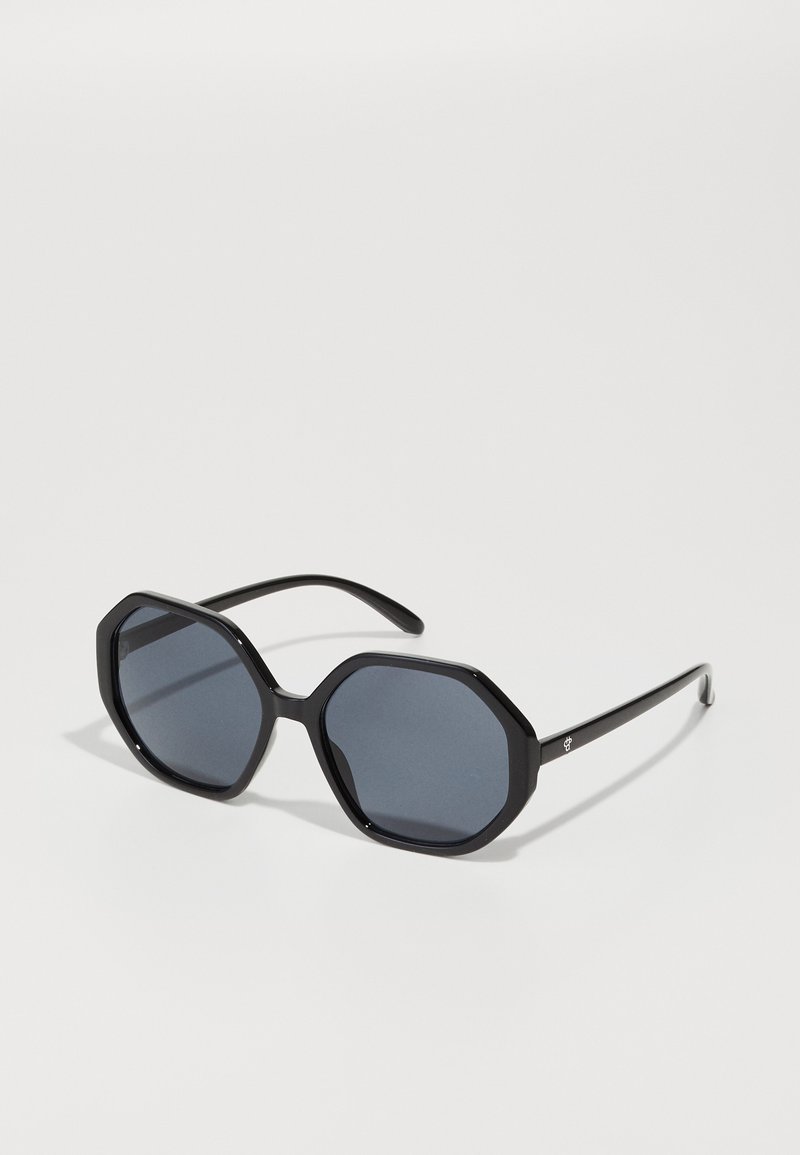 Ochelari de soare octagonali negri cu lentile întunecate. Ramă din plastic elegantă, cu textură netedă și brațe subțiri, având un mic logo pe o parte.