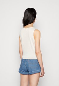 Světlé béžové žebrované bezrukávové tričko v kombinaci s srolovanými denimovými šortkami. Tričko má kulatý výstřih a hladkou texturu; šortky mají klasické zadní kapsy.