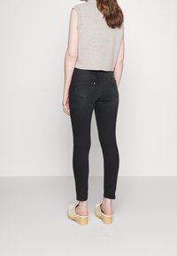 Jeans ajustados negros de cintura alta, con bolsillos traseros y detalles sutiles. Combinados con una blusa de punto sin mangas de color gris claro y zuecos de madera.
