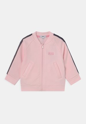 Chaqueta rosa con cremallera y detalles en azul marino, con bolsillos laterales, cuello y puños acanalados. Logotipo bordado en el pecho. Tejido suave.