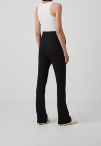Černé rozšířené kalhoty vyrobené z texturovaného pleteného materiálu, s přiléhavým pasem a hladkým povrchem, společně s bílou obuví.