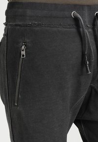 Svarta joggers i mjukt tyg, med ribbad midja, dragsko och en ficka med dragkedja på sidan för förvaring.