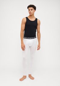 Svart tank topp og hvite leggings, tettsittende design med en glatt tekstur. Leggingsene har en merket midjebånd med "CK & JONES."