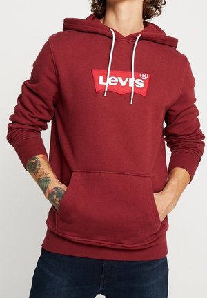 Sudadera color burdeos con un bolsillo canguro al frente, cordones blancos y un parche del logo de Levi's rojo en el pecho. Material de algodón, diseño casual.