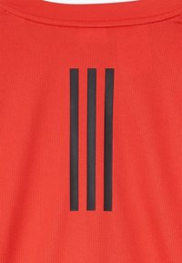 Červená texturová tkanina se třemi vertikálními černými pruhy, které jsou umístěny pod kulatým výstřihem.