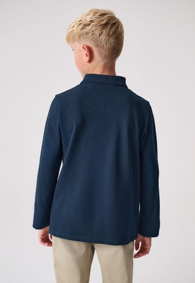 Tengerészkék hosszú ujjú galléros póló puha textúrával és gallérral. Látható varrás a nyakvonal és az alja mentén, minimalista dizájn.