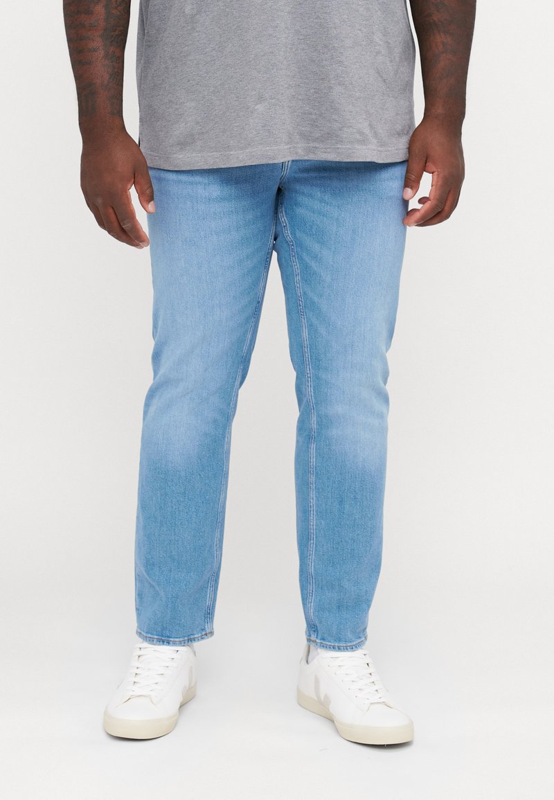 Jeans in denim azzurro chiaro con vestibilità dritta, caratterizzati da un lavaggio sbiadito e design a cinque tasche standard, abbinati a sneakers bianche.