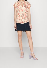 Blusa floreale in tonalità pesca e rosa, con maniche corte e scollatura a chiave. Abbinata a una gonna plissettata nera e sandali con tacco a blocco lavanda.