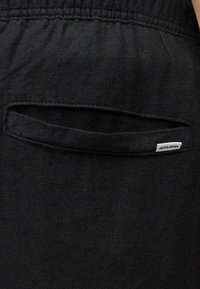 Κοντινό πλάνο τσέπης μαύρου υφασμάτινου παντελονιού με ελαστική μέση και μικρή λευκή ετικέτα "JACK & JONES" στην άκρη της τσέπης.