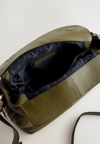 Õliva rohelise tekstuuri ja ehtnahast käekott, mis on avatud ning paljastab tume kanga voodri ja seesmist lukuga taskut.